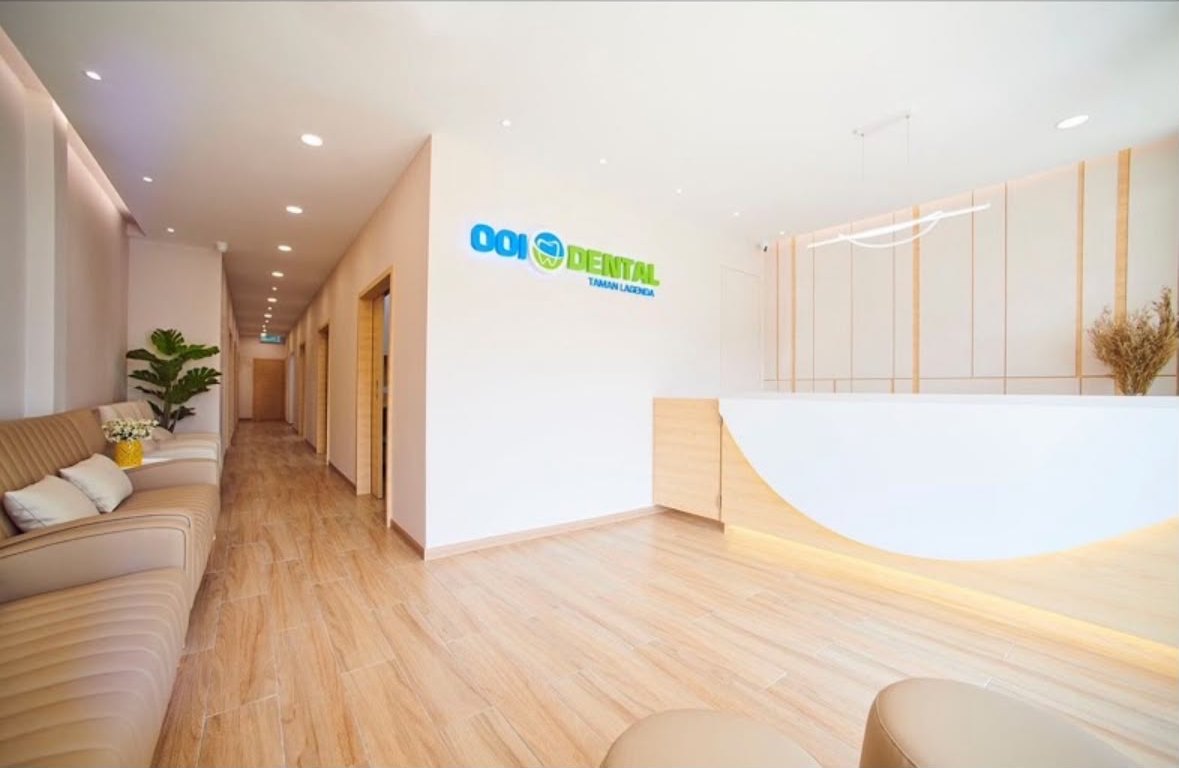 The reception at OOI Dental Taman Lagenda: light oak floor, a curved white counter, and the clinic wordmark lit on the far wall