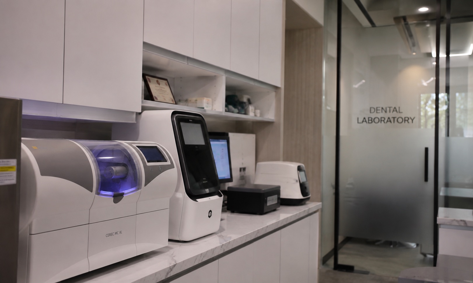 The in-house dental laboratory at OOI Dental: a CEREC MC XL milling unit with its chamber lit, a 3D printer and scanner on the bench, and the glass door marked Dental Laboratory behind