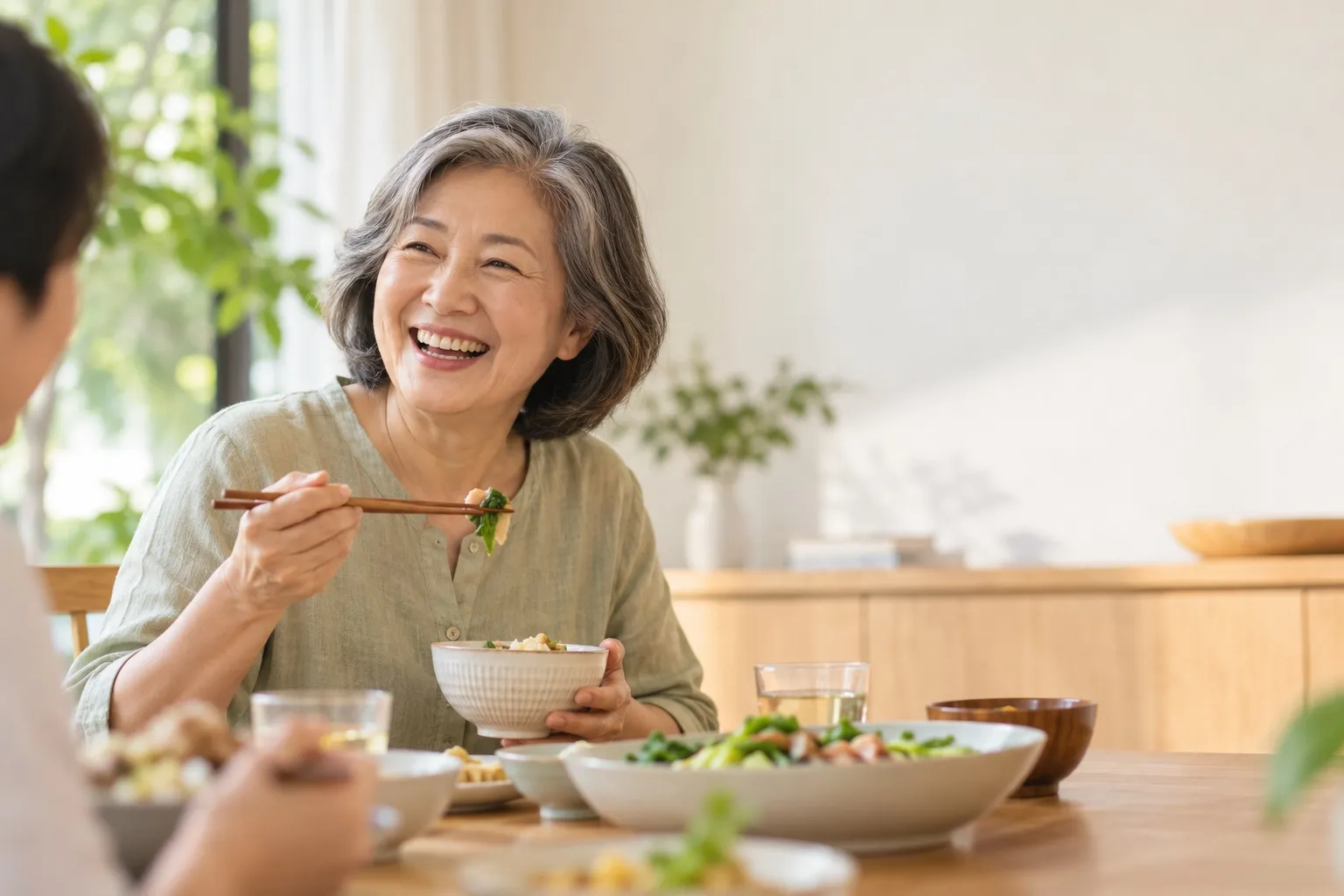 An older woman laughing with her family while eating at the dinner table